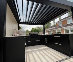  Bespoke metal outdoor kitchen with a metal pergola overhead. Porcelain paving.