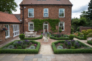  Central view of the rear of a traditional house with formal beds using box hedging and structural planting and brick paving.