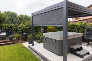  Hot tub standing on external porcelain paving covered using a metal pergola with remote side screens.