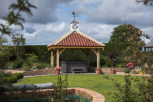  a hot tub covered with a tiled roof oak structure within a garden setting surrounded by natural planting.