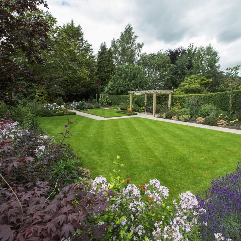 Large traditional garden with lawn and timber pergola.