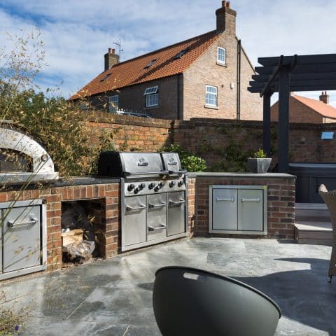 Outdoor kitchen using stainless BBQ and pizza oven in a modern garden