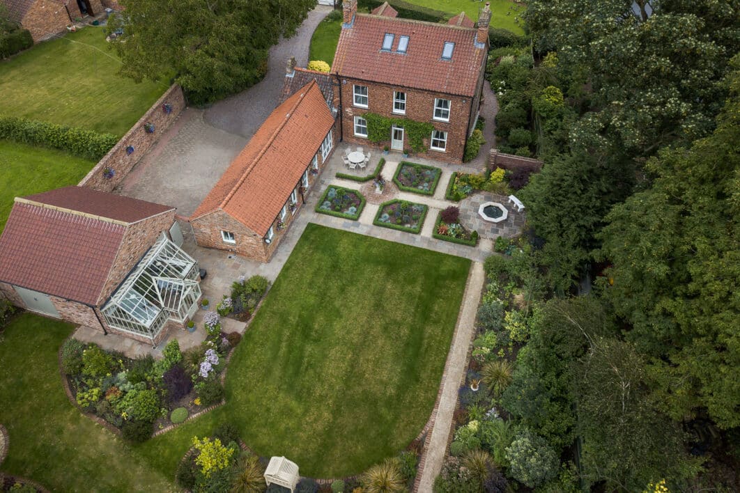 Aerial view of formal riverside garden with manicured lawns, structured planting beds, greenhouse and summerhouse.