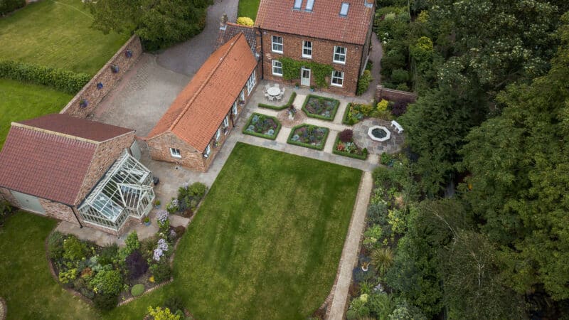 Aerial view of formal riverside garden with manicured lawns, structured planting beds, greenhouse and summerhouse.